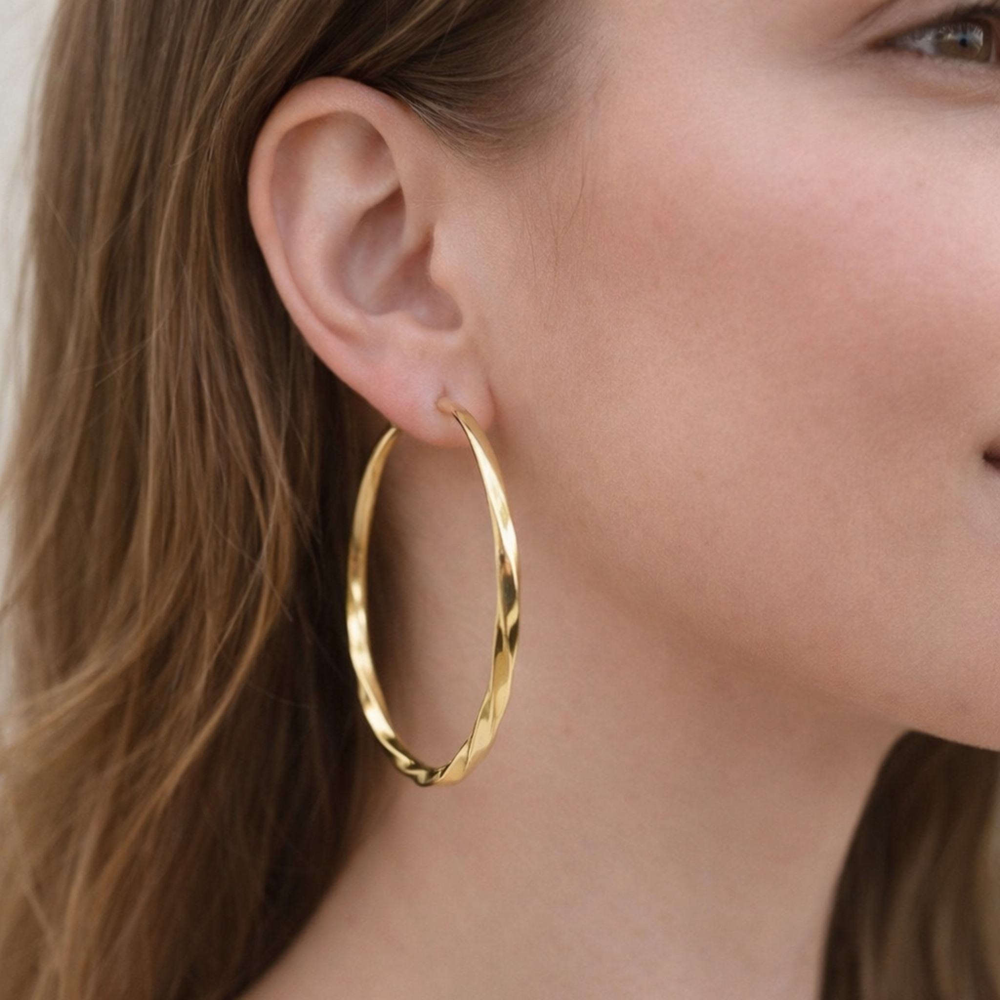 Gold hoop earring worn by a person with a neutral background