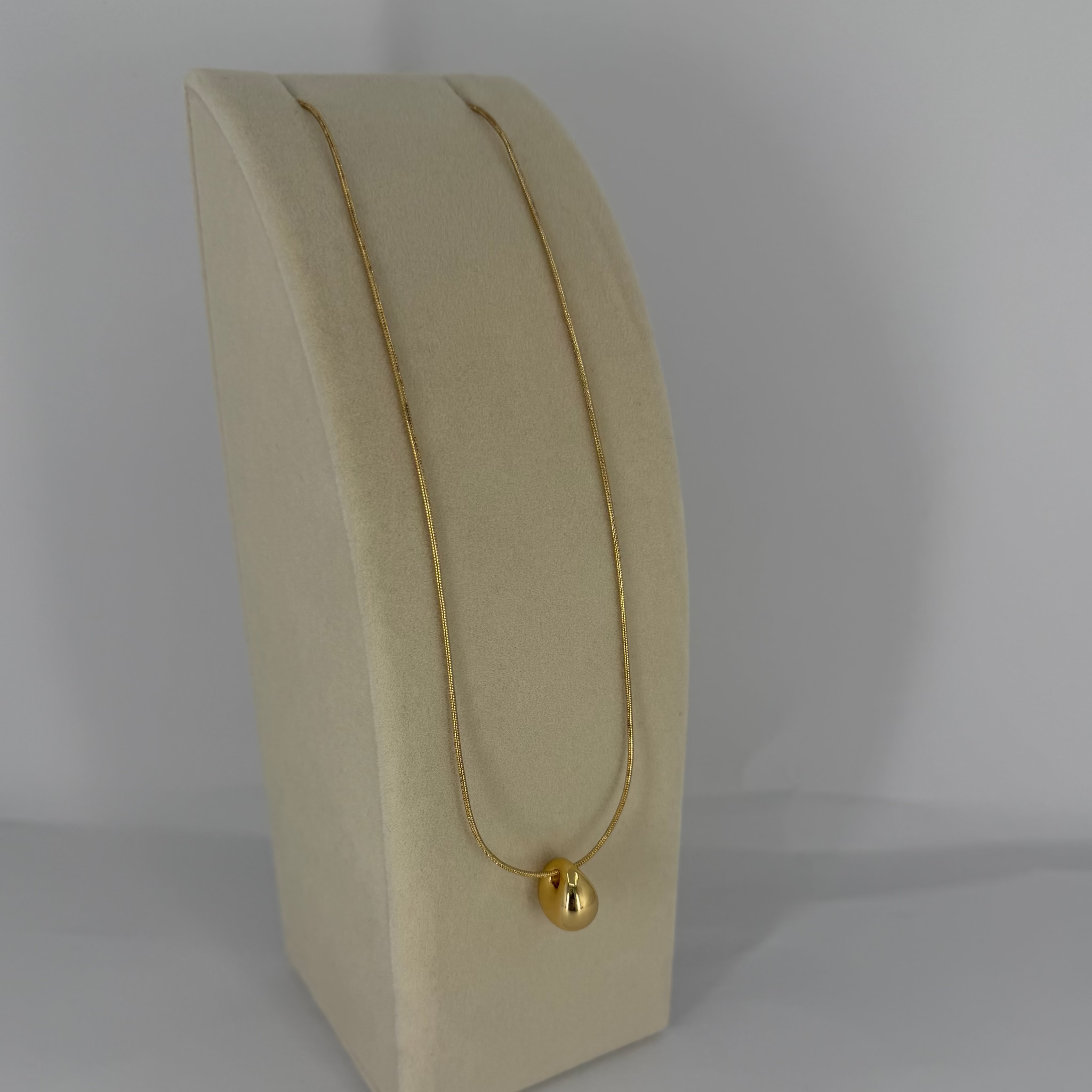 Gold necklace on a beige jewelry display stand against a gray background