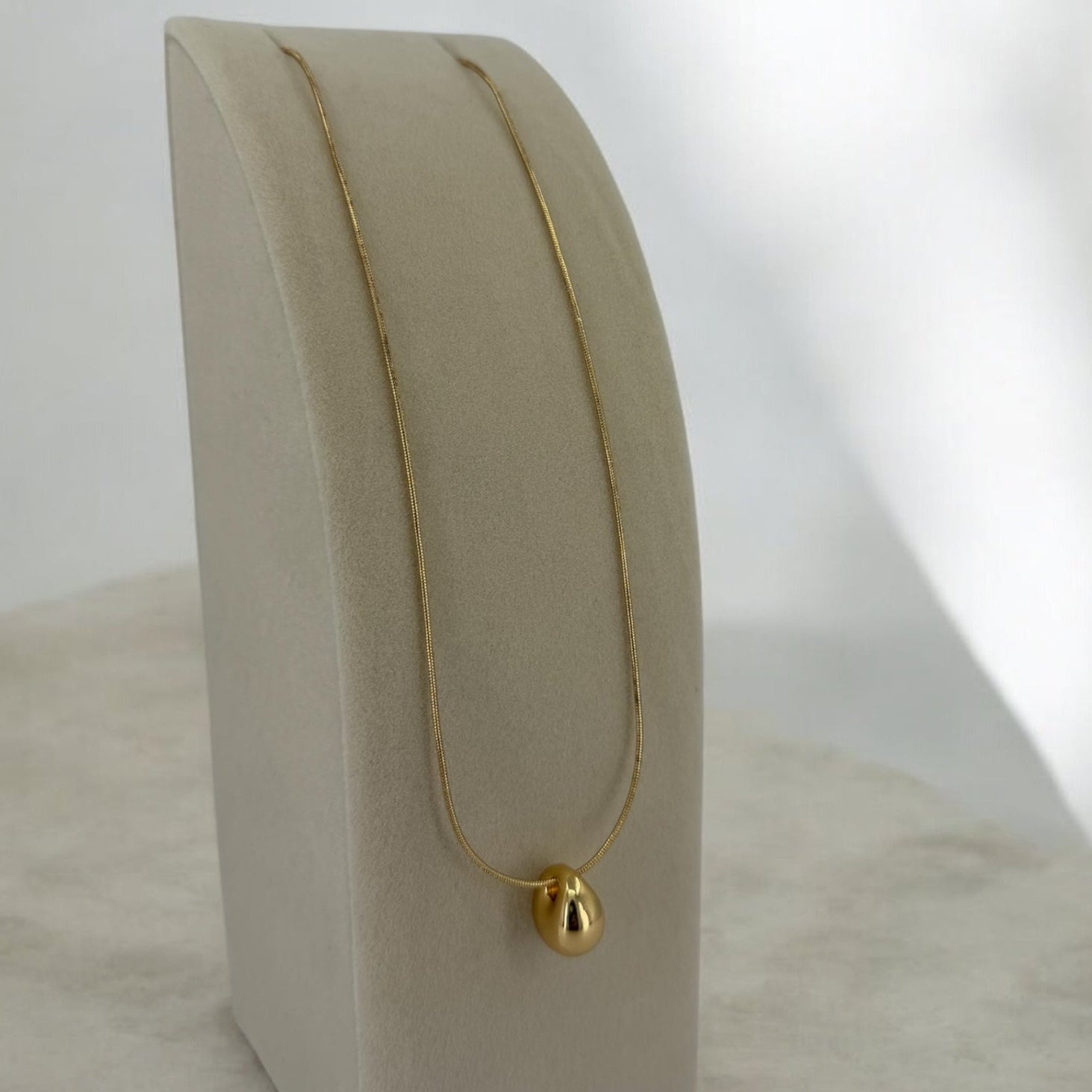 Gold necklace on a beige jewelry display stand against a white background