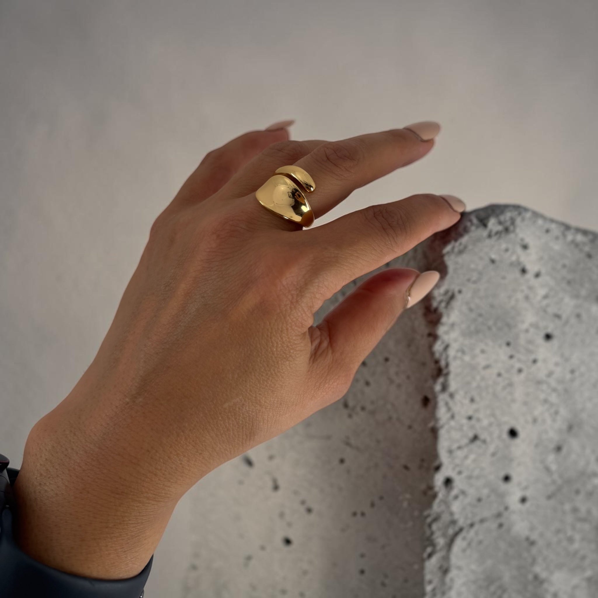 Hand wearing a gold ring on a textured surface