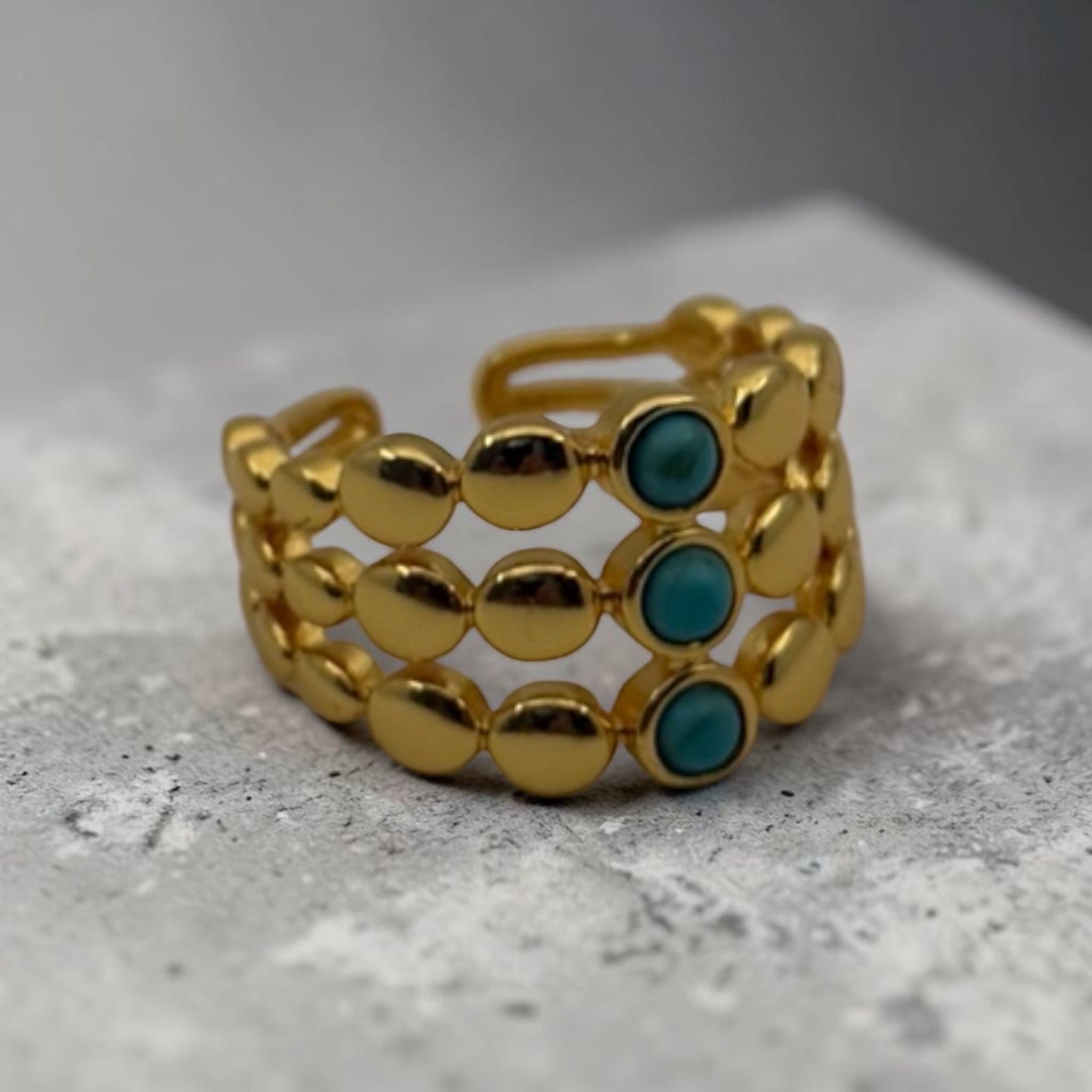 Gold ring with turquoise stones on a textured surface