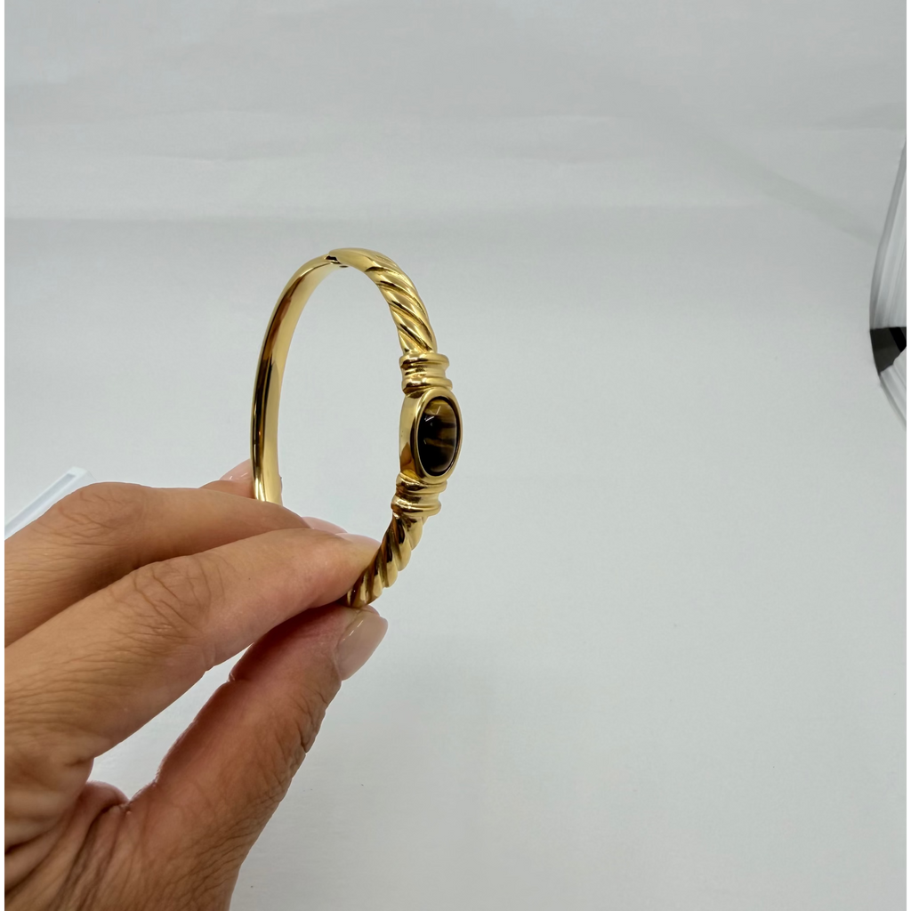 A gold bangle bracelet with a twisted rope design and a central oval amber stone