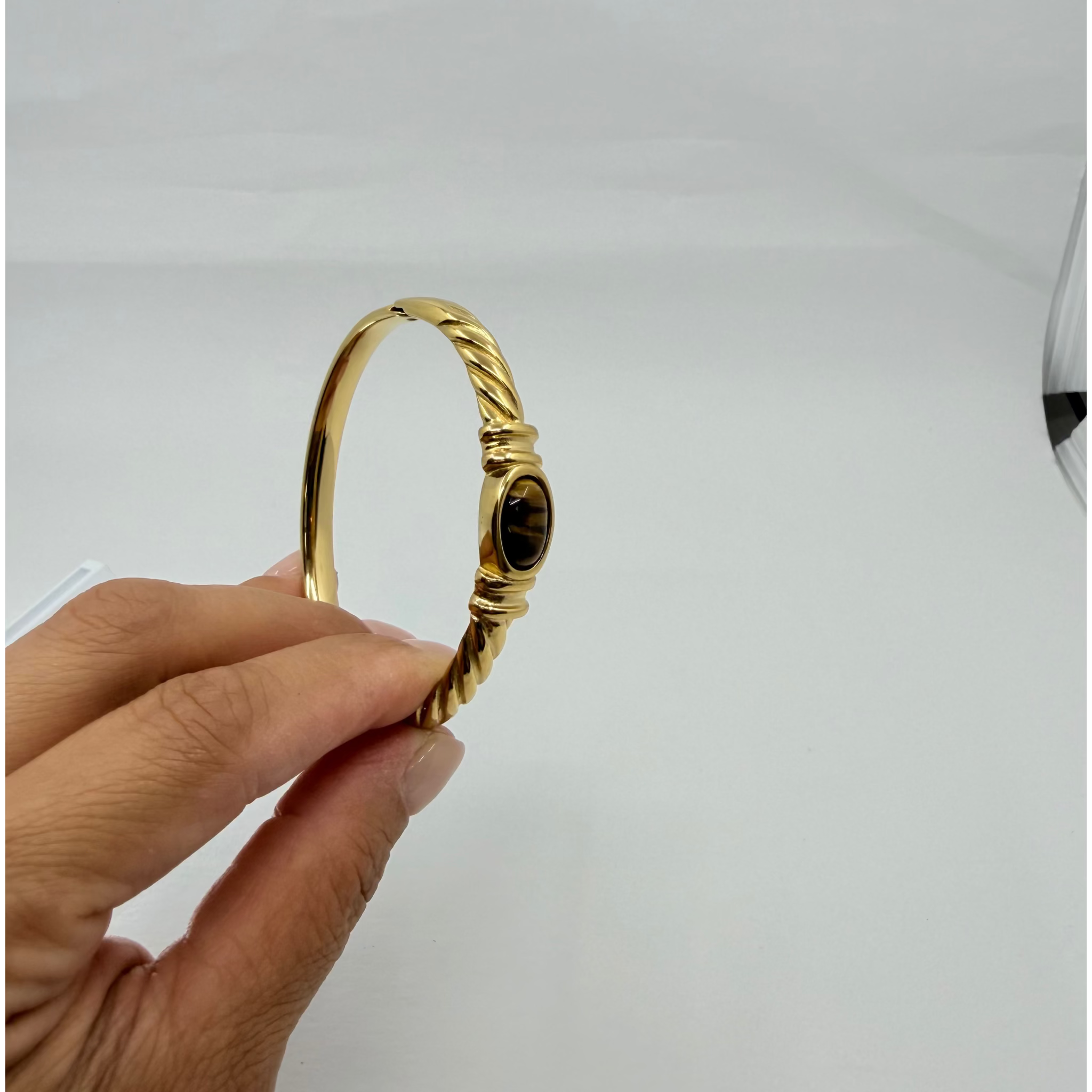 A gold bangle bracelet with a twisted rope design and a central oval amber stone
